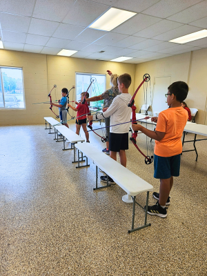 four kids learning archery in the 4h building 